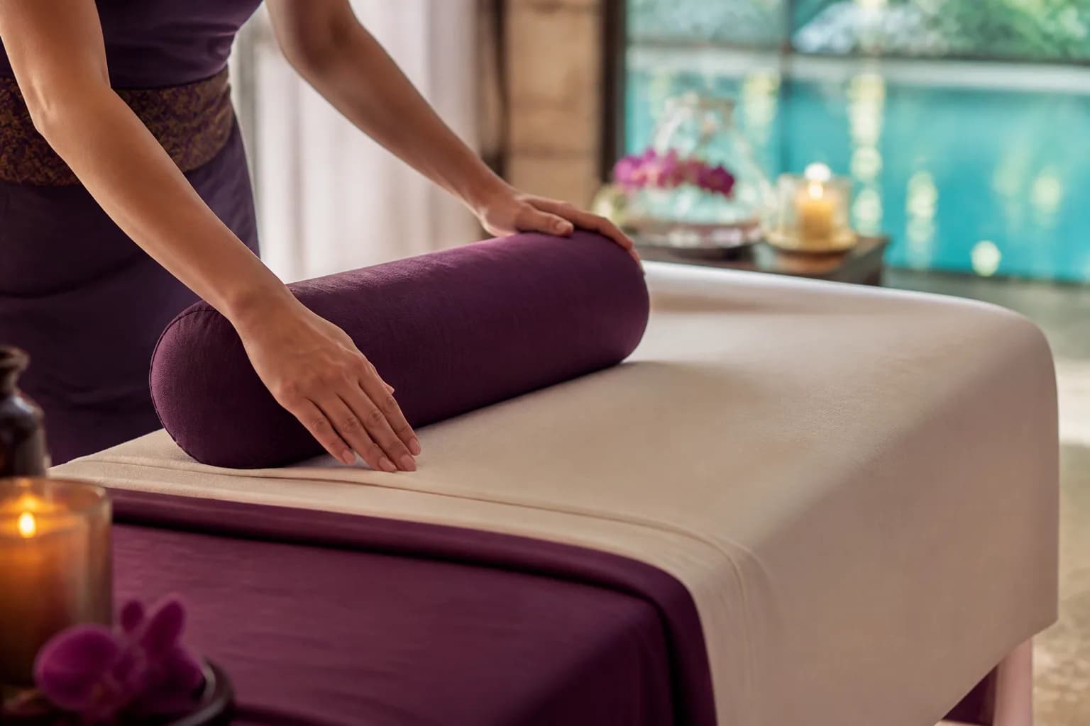Anonymous therapist hands preparing fresh cream linens and a plum bolster on an empty massage table